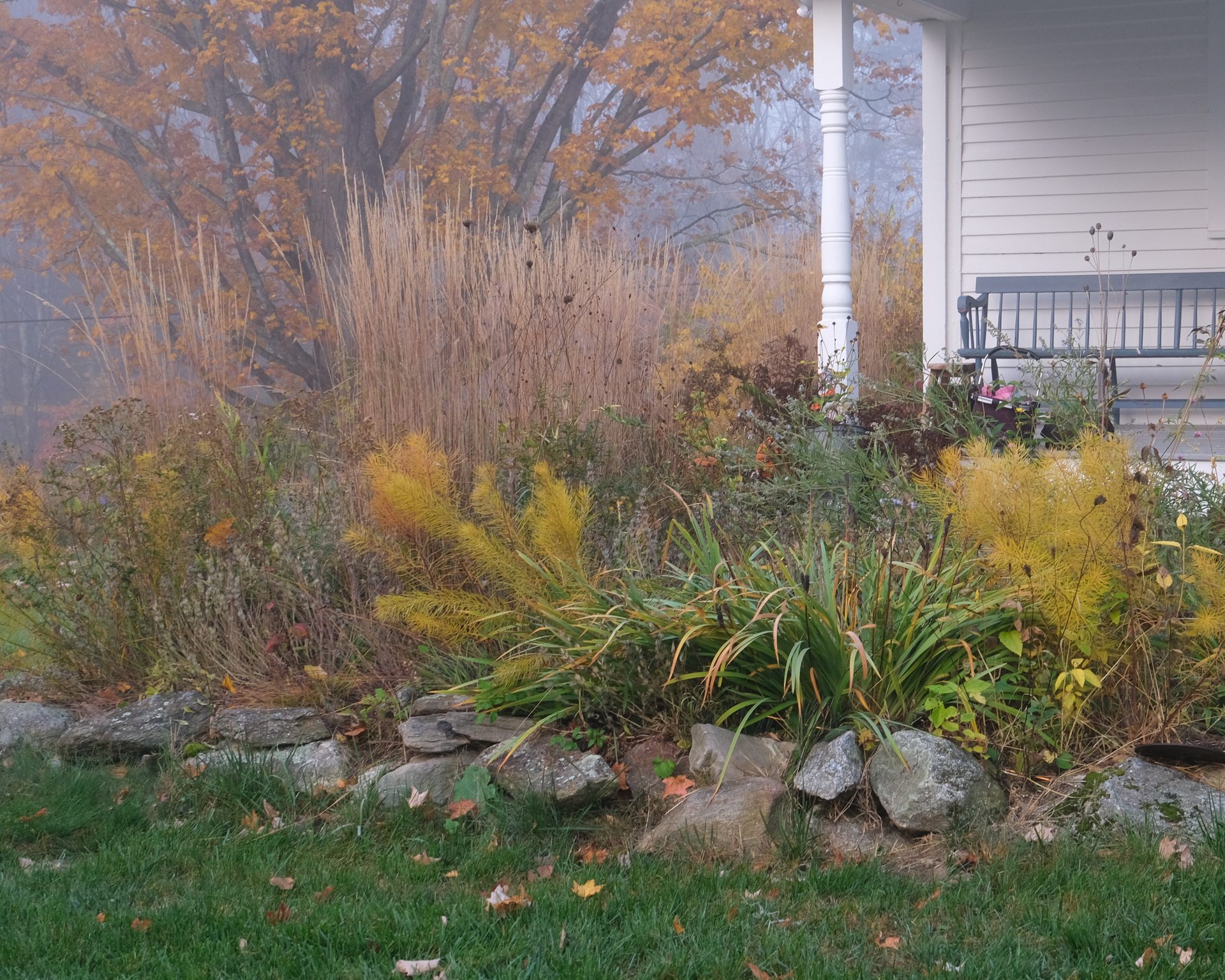 Residential garden with stone wall and porch in fall, New Hampshire